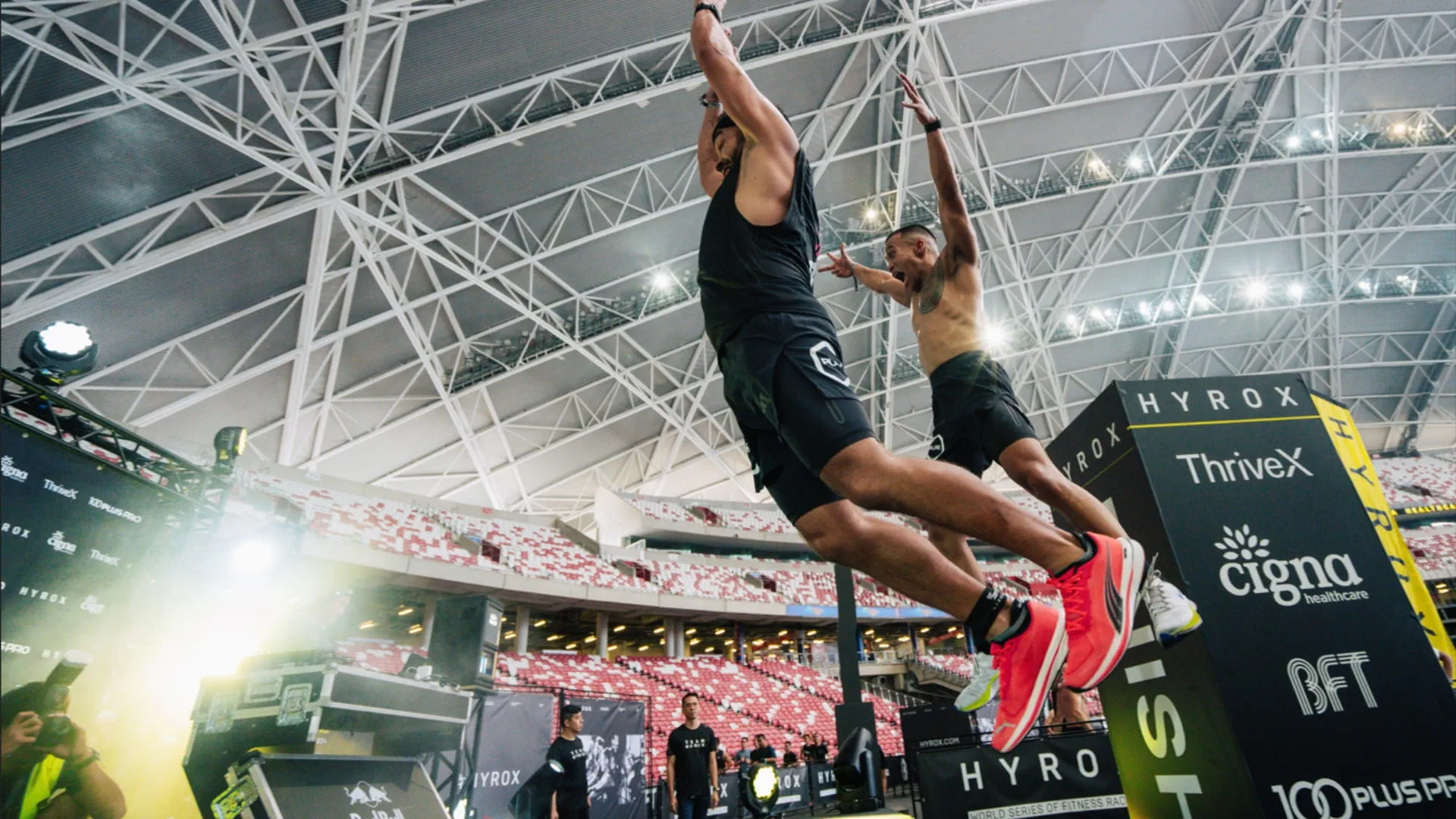 Athletes mid-air during burpee broad jumps at a Hyrox competition
